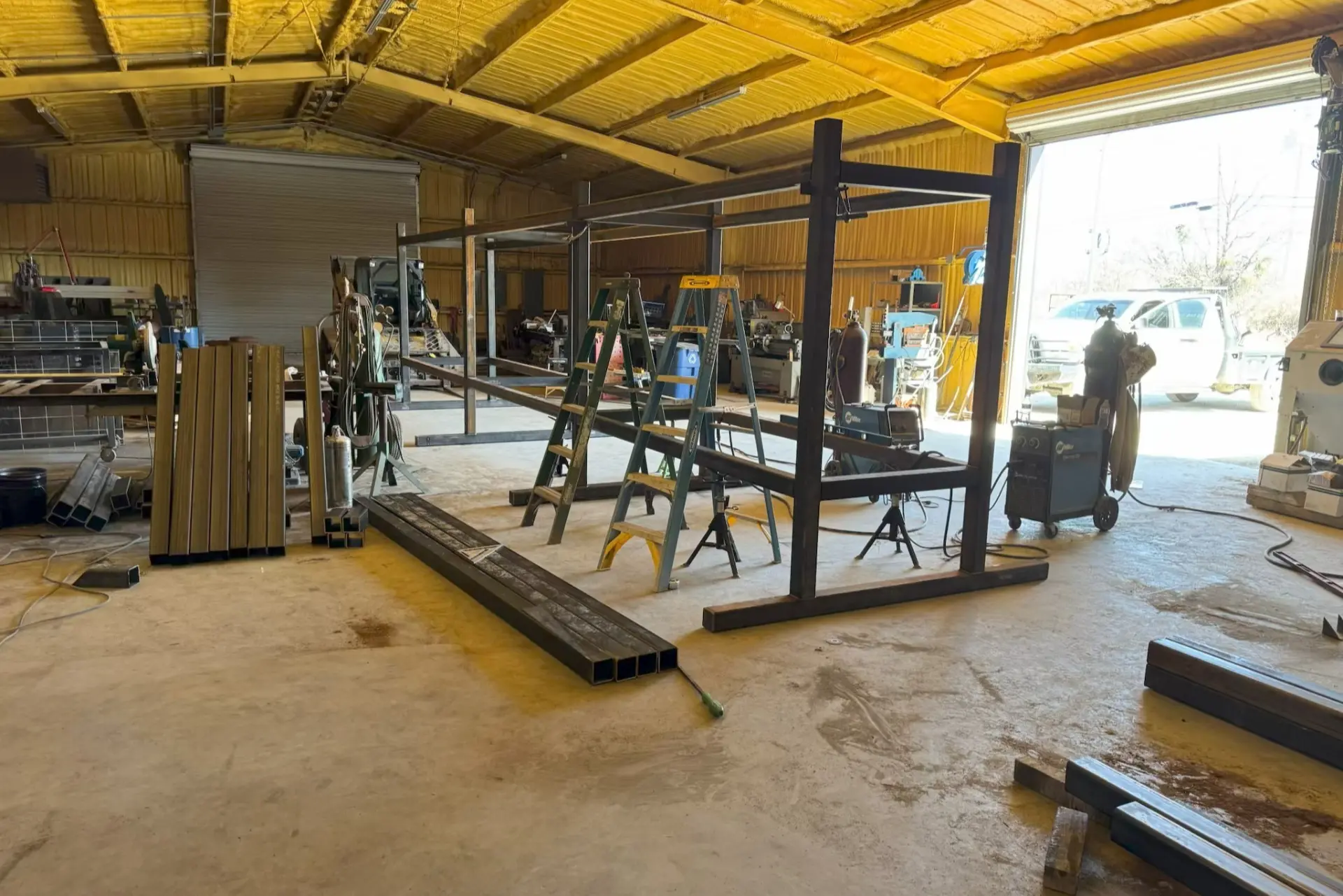 A workshop with a yellow, insulated ceiling features a metal frame structure under construction.